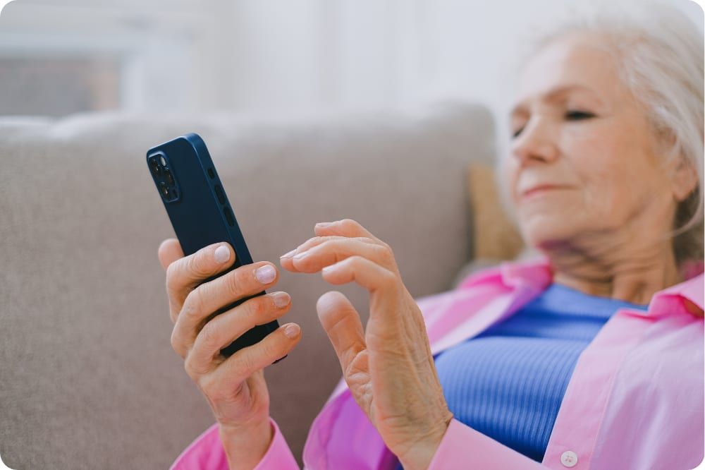 Ältere Frau sitzt auf einem Sofa und tippt auf ihrem Smartphone
